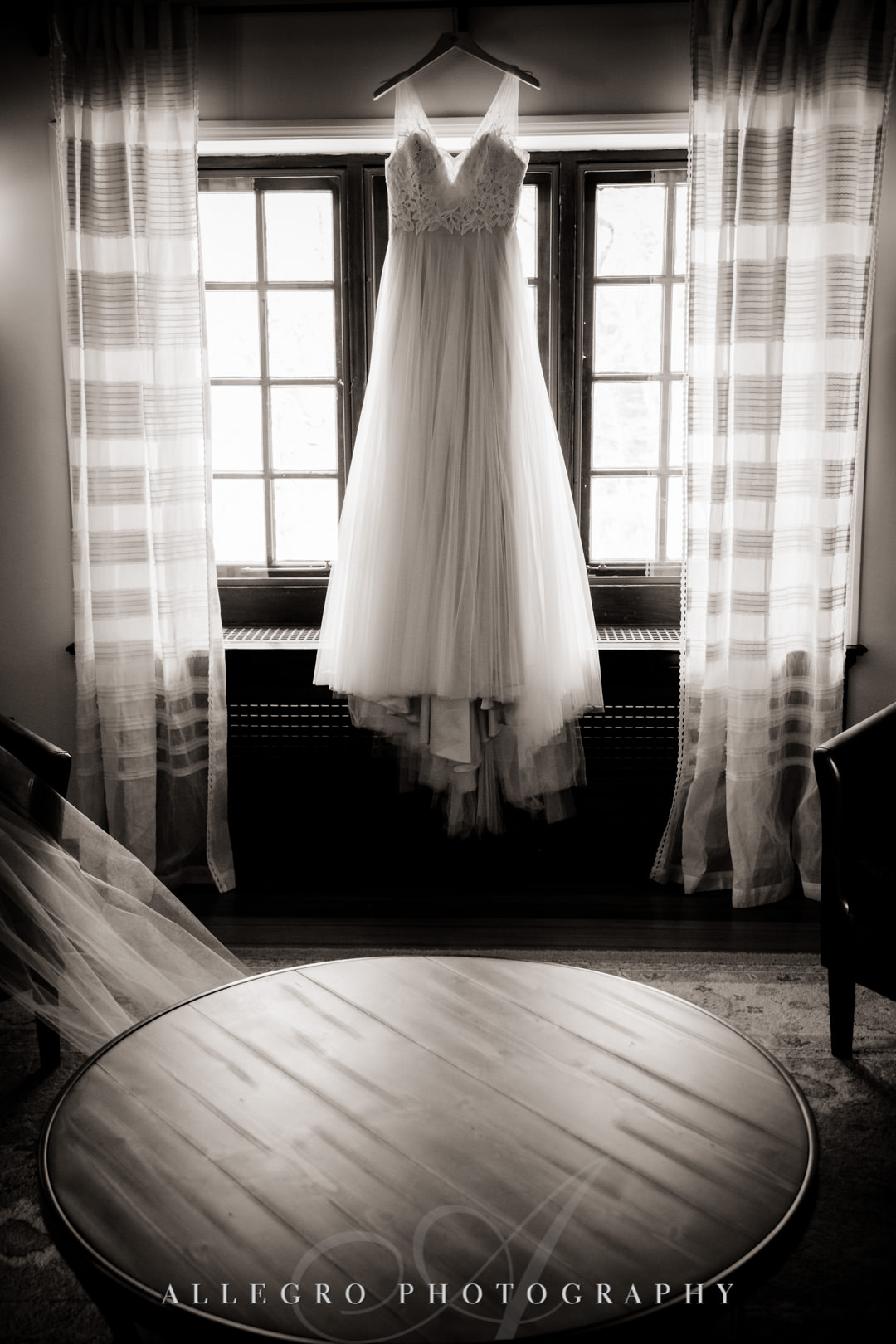 Black and white photo of wedding dress hanging in sunlit room.