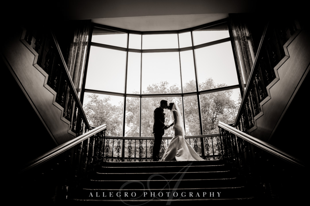 Black and white photo of newlyweds kissing atop a staircase | Allegro Photography