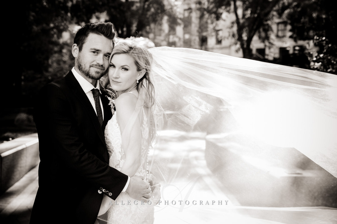 bride and groom in black and white with veil blowing in the wind